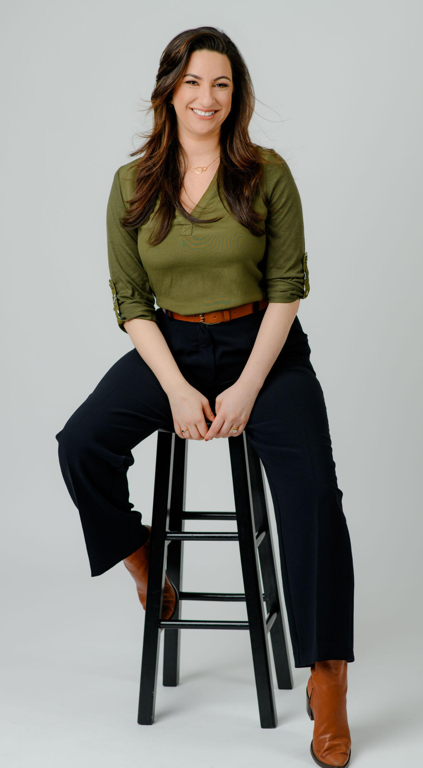 Lauren Fagan sitting in a green shirt with black pants and a brown belt on a stool.